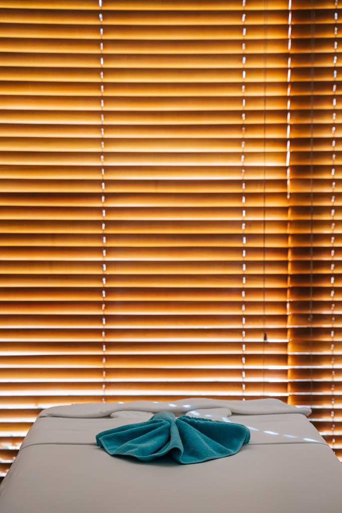 A serene spa setting featuring a massage table with teal towel and wooden window blinds.